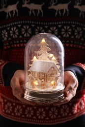 Man in Christmas sweater holding decorative snow globe, closeup