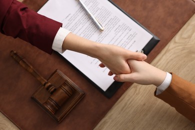 Notary shaking hands with client at wooden table, top view