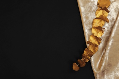 Photo of Gold painted eucalyptus branch and fabric on black background, top view with space for text