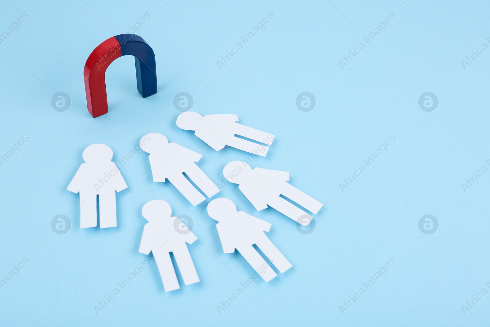 Photo of Magnet attracting paper people on light blue background