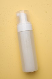 Photo of Wet bottle of face cleansing product on pale orange background, top view