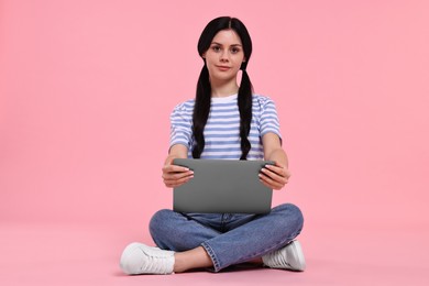 Student with laptop sitting on pink background