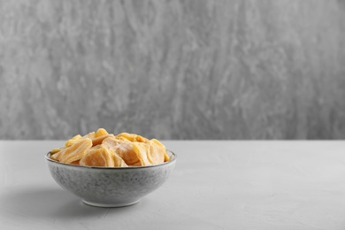 Photo of Delicious dried jackfruit slices in bowl on grey table. Space for text