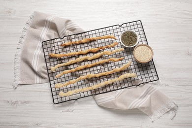 Photo of Rack with homemade breadsticks and spices on white wooden table, flat lay. Cooking traditional grissini