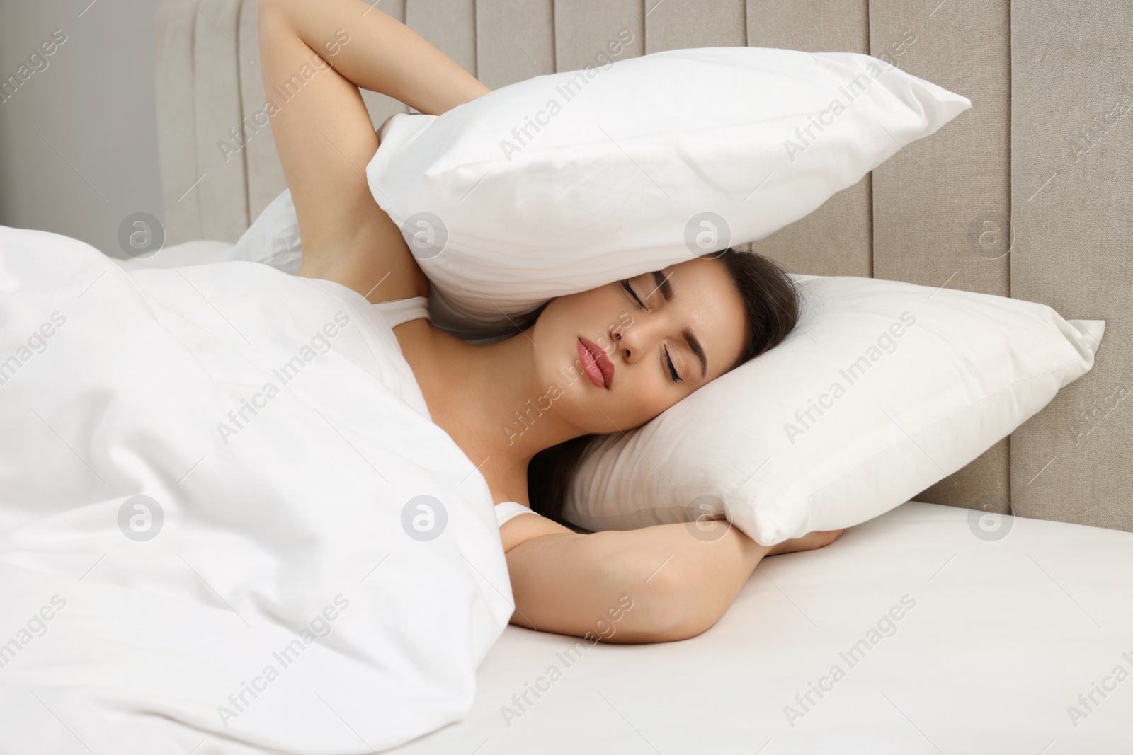 Photo of Unhappy young woman covering ears with pillows in bed