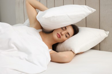Photo of Unhappy young woman covering ears with pillows in bed