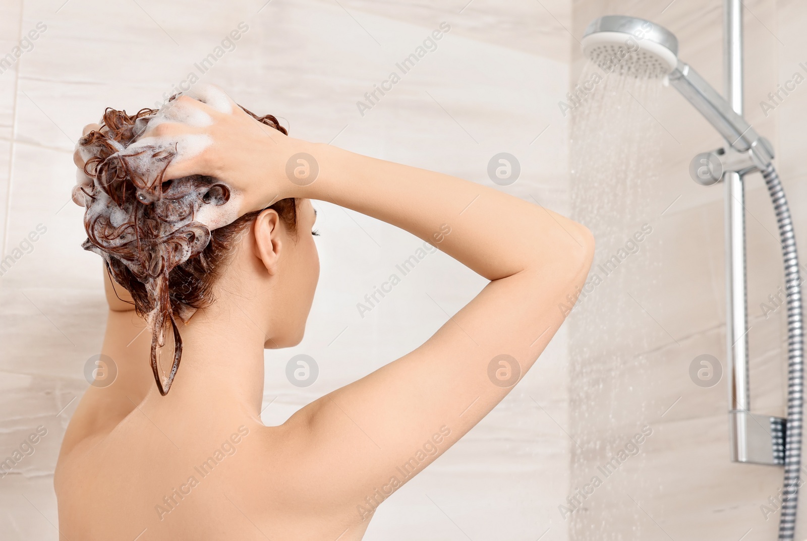 Photo of Young woman washing her hair with shampoo in shower, back view