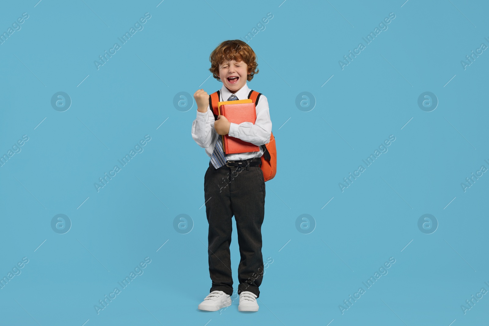 Photo of Happy schoolboy with backpack and books on light blue background