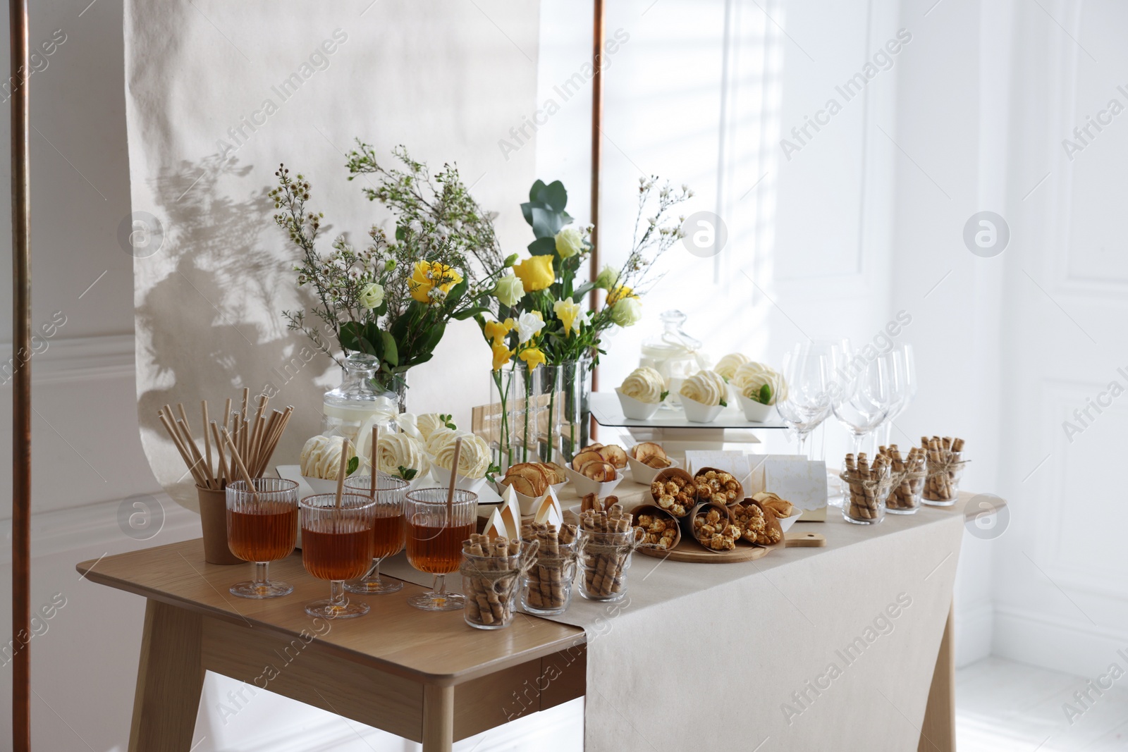 Photo of Delicious treats and glasses of drink on wooden table in room. Sweet buffet