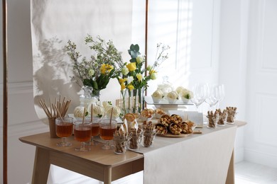 Delicious treats and glasses of drink on wooden table in room. Sweet buffet