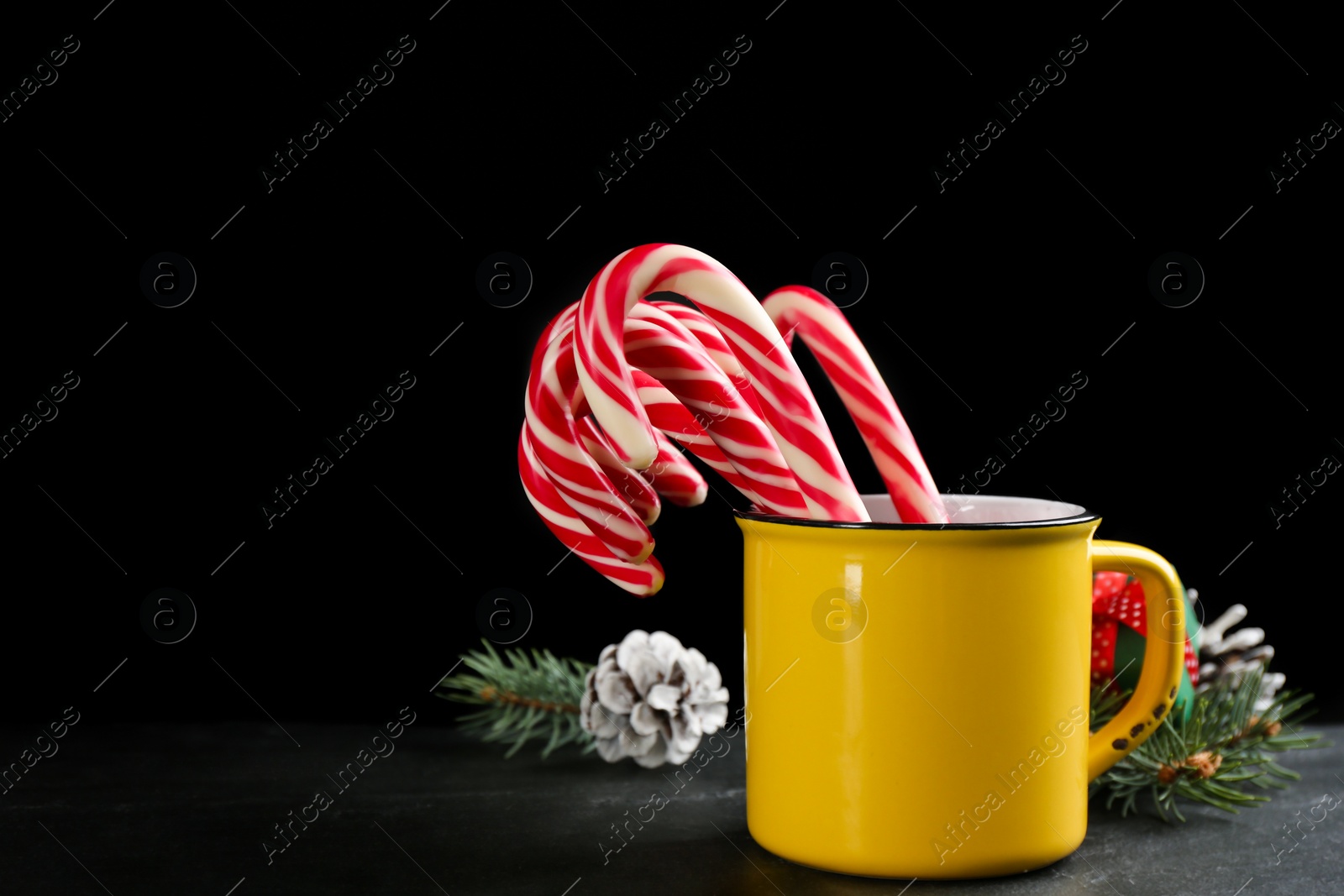 Photo of Christmas candy canes in cup on black table against dark background, space for text