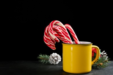 Christmas candy canes in cup on black table against dark background, space for text