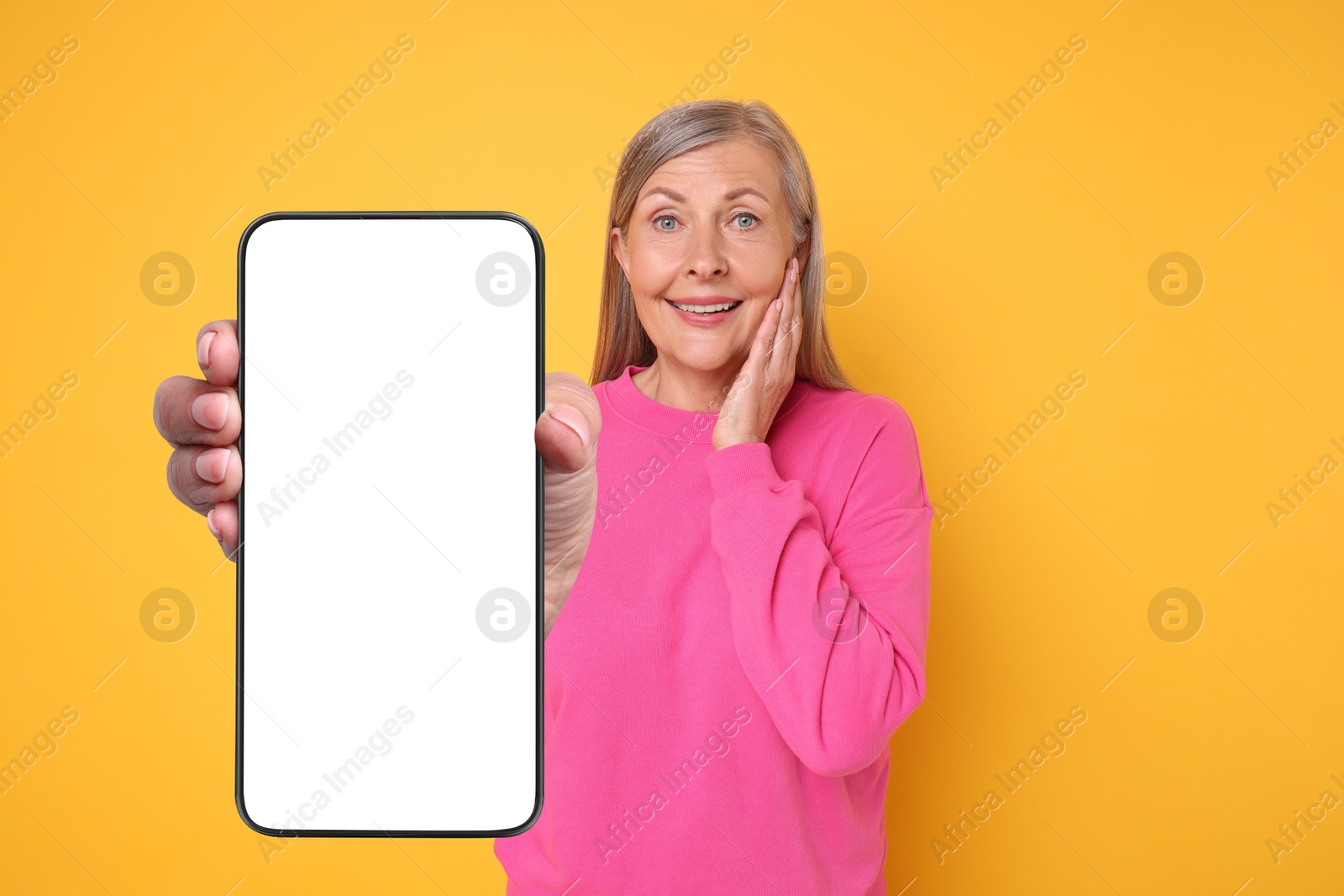 Image of Happy mature woman showing mobile phone with blank screen on golden background. Mockup for design