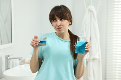 Photo of Young woman using mouthwash in bathroom. Oral hygiene