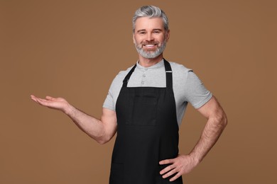 Photo of Happy man wearing kitchen apron on brown background. Mockup for design