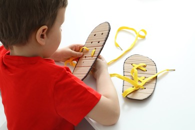 Photo of Little boy tying shoe laces using training cardboard template at white table