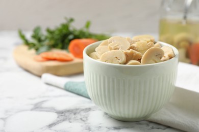 Photo of Delicious marinated mushrooms in bowl on white marble table. Space for text