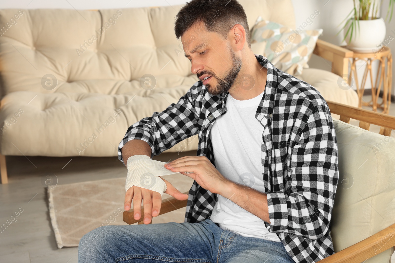 Photo of Man applying medical bandage onto hand at home