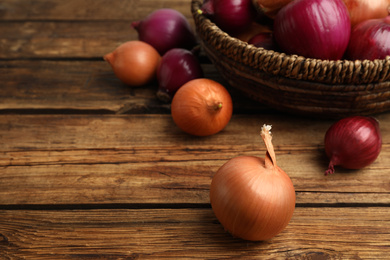 Photo of Onion bulbs and basket on wooden table. Space for text