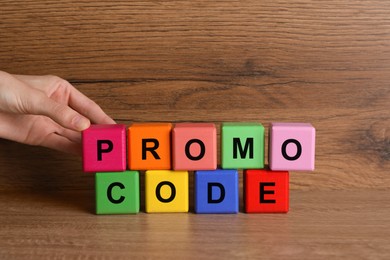 Photo of Woman making words Promo Code with colorful cubes at wooden table, closeup
