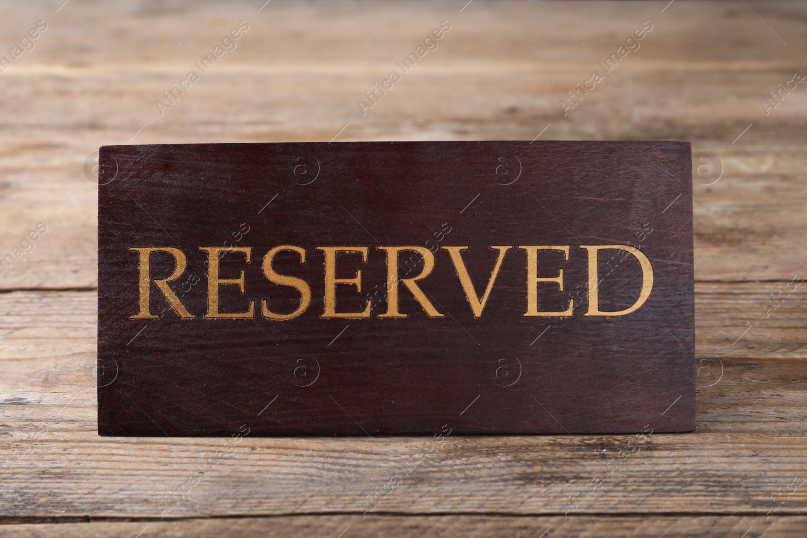 Photo of Elegant sign RESERVED on wooden surface. Table setting element