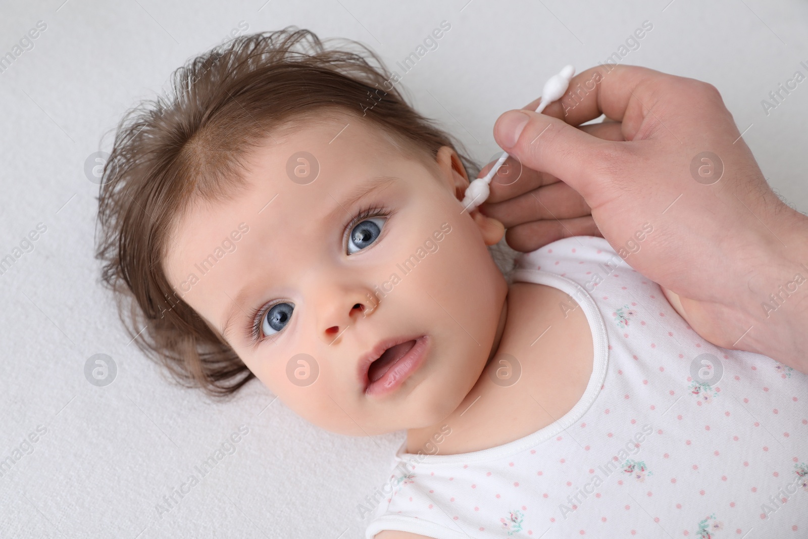 Photo of Father cleaning ear of his baby with cotton bud on bed, closeup