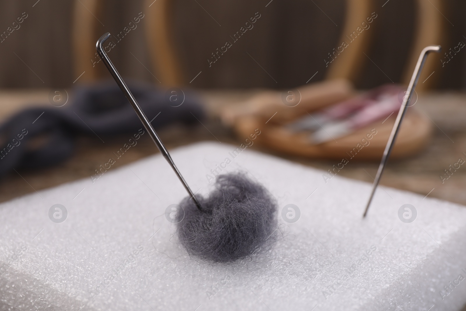 Photo of Grey felting wool, pad and needles on table, closeup