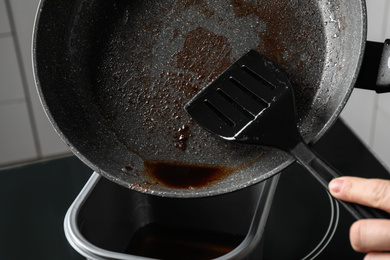 Photo of Woman pouring used cooking oil from frying pan into container, closeup