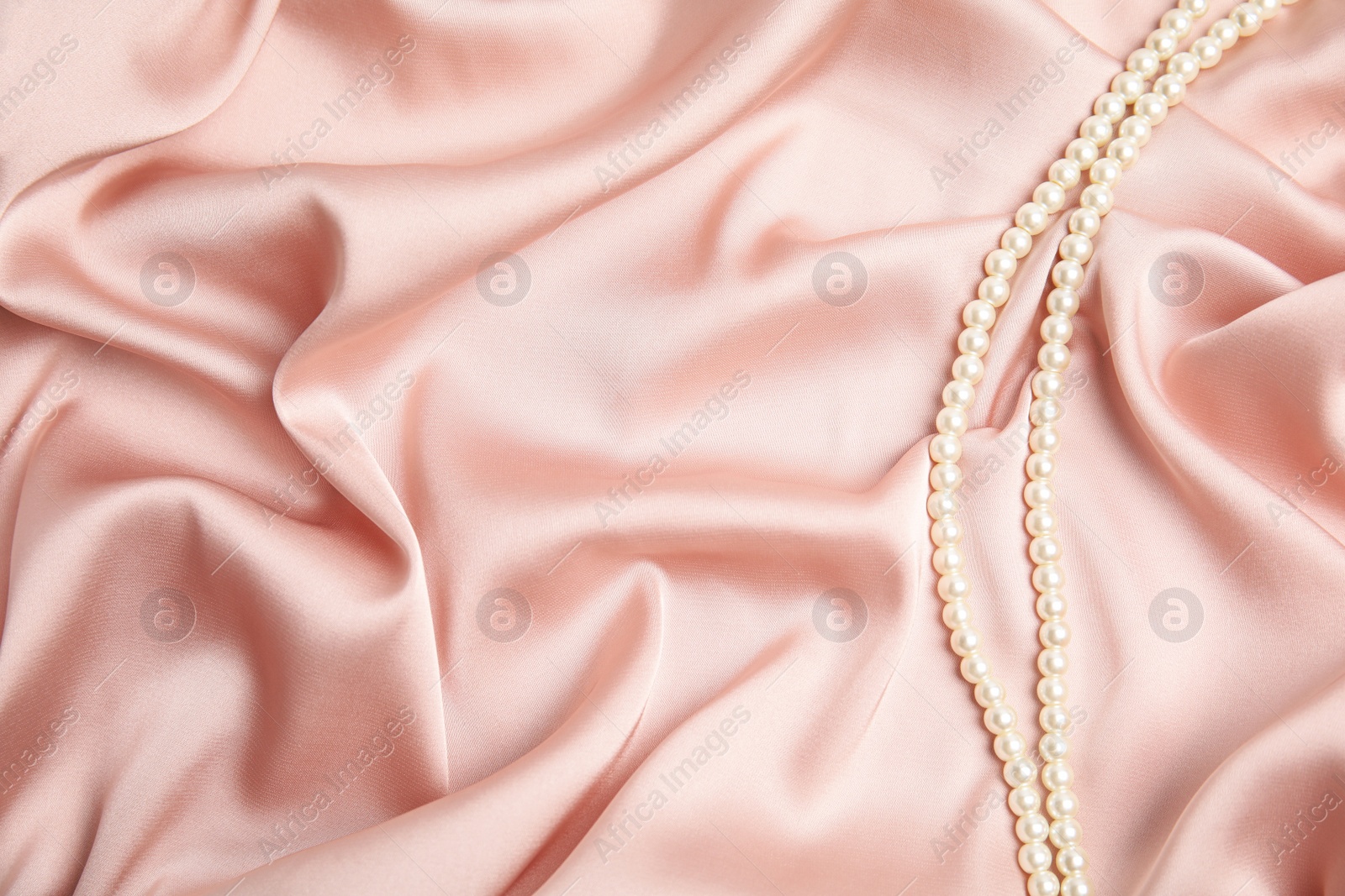 Photo of Beautiful pearls on pink silk, top view. Space for text