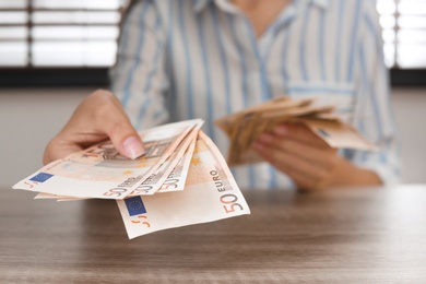 Photo of Woman with Euro banknotes at wooden table indoors, closeup