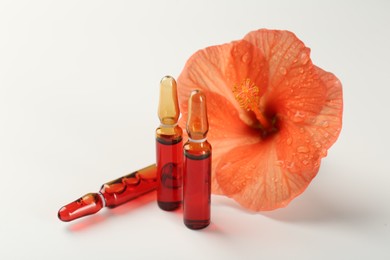 Skincare ampoules and hibiscus flower on white background