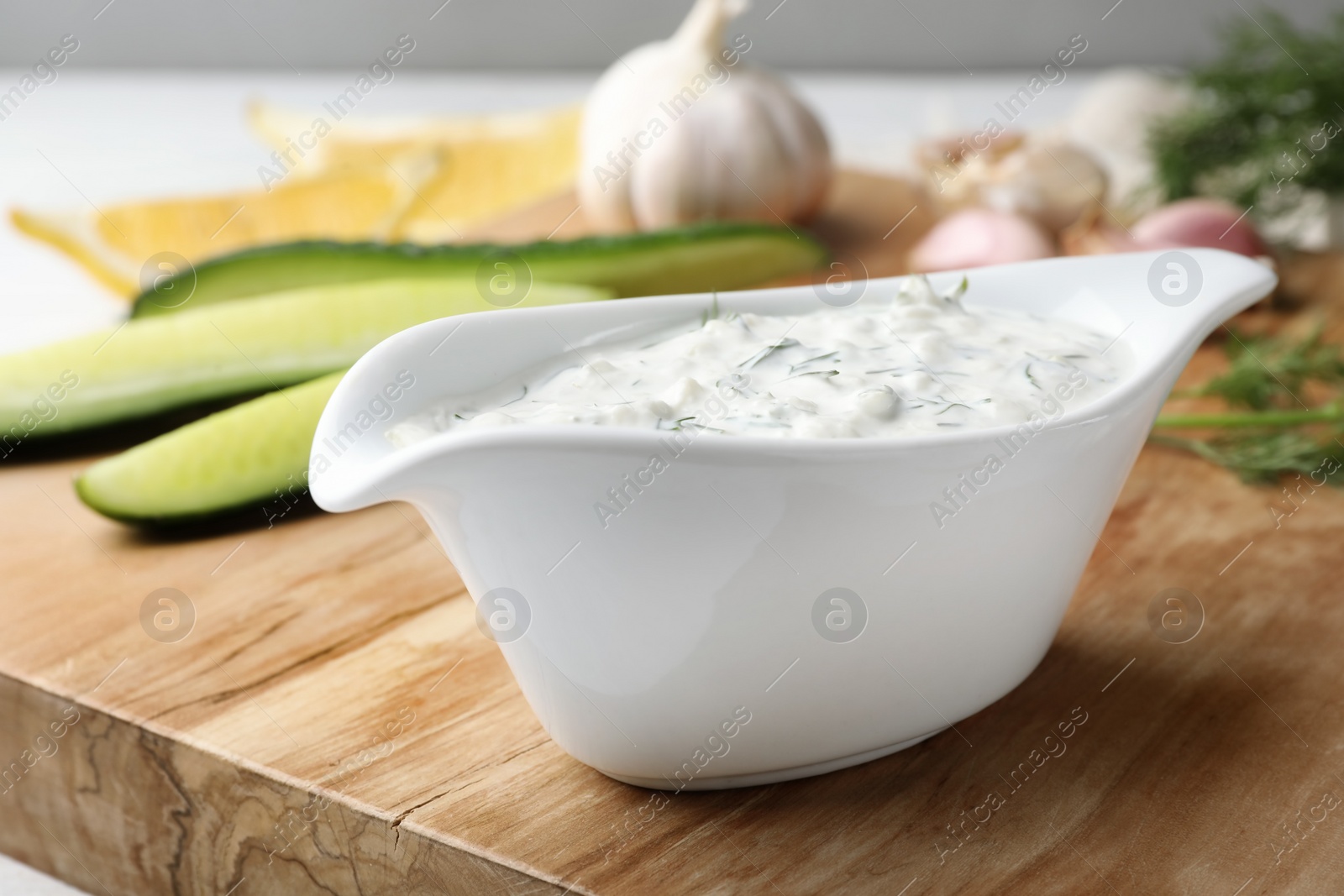 Photo of Cucumber sauce with ingredients on wooden board. Traditional Tzatziki