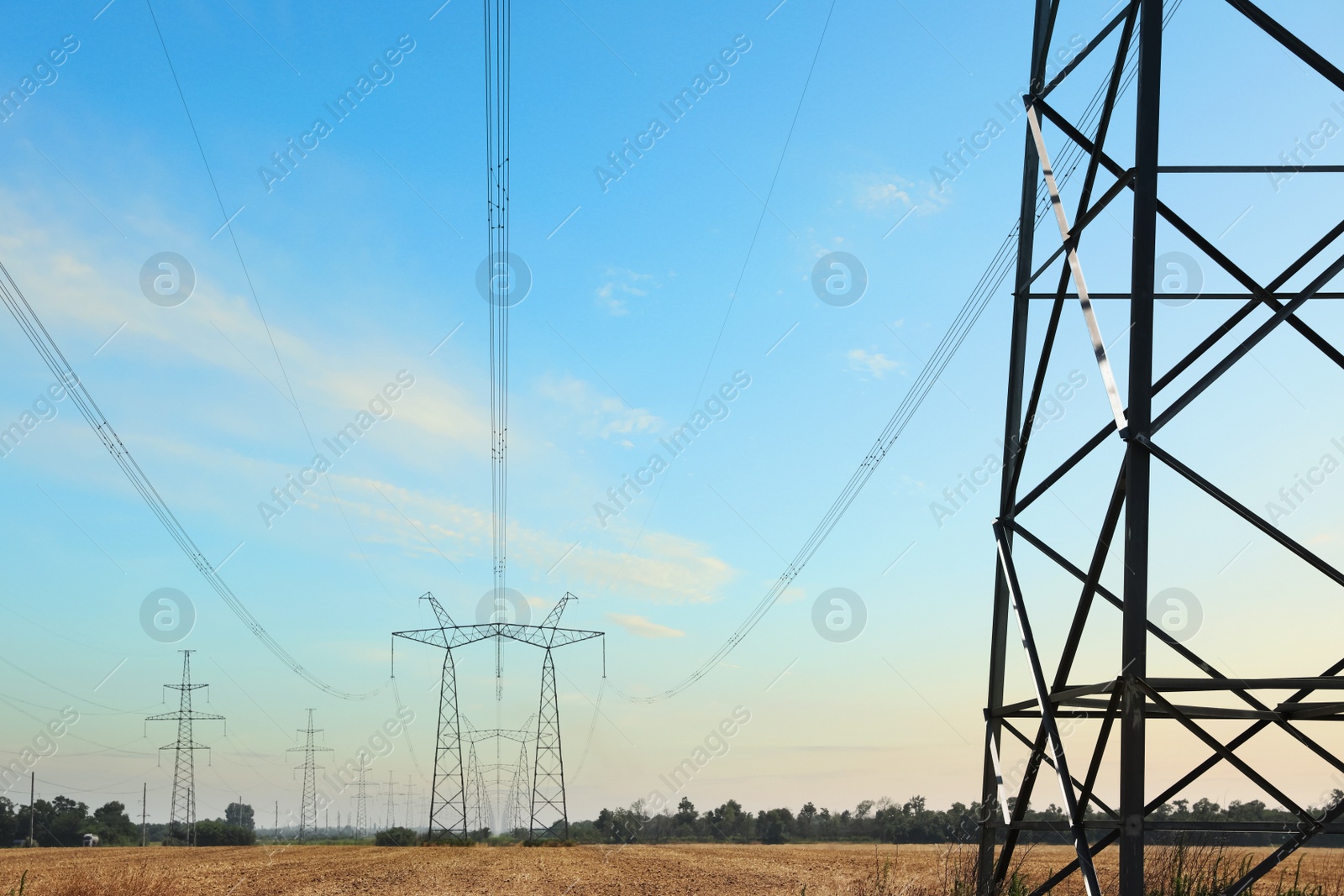 Photo of High voltage towers with electricity transmission power lines in field on sunny day