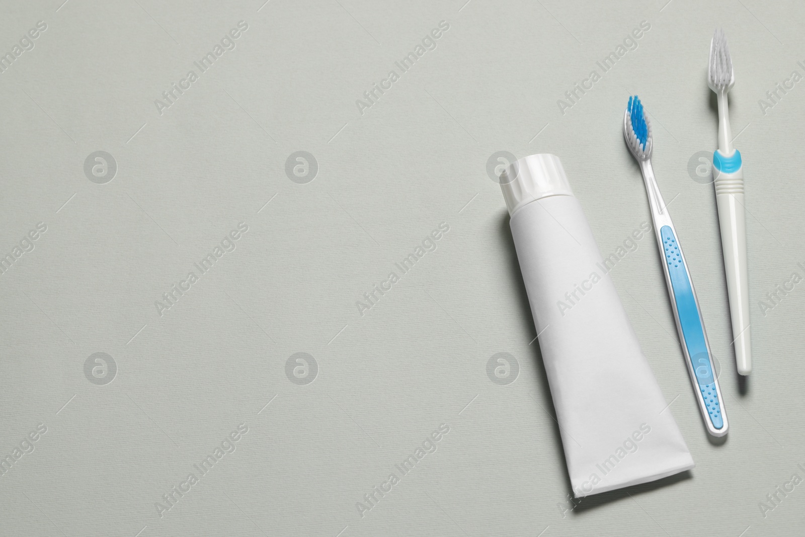 Photo of Plastic toothbrushes and paste on grey background, flat lay. Space for text