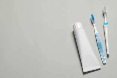 Plastic toothbrushes and paste on grey background, flat lay. Space for text