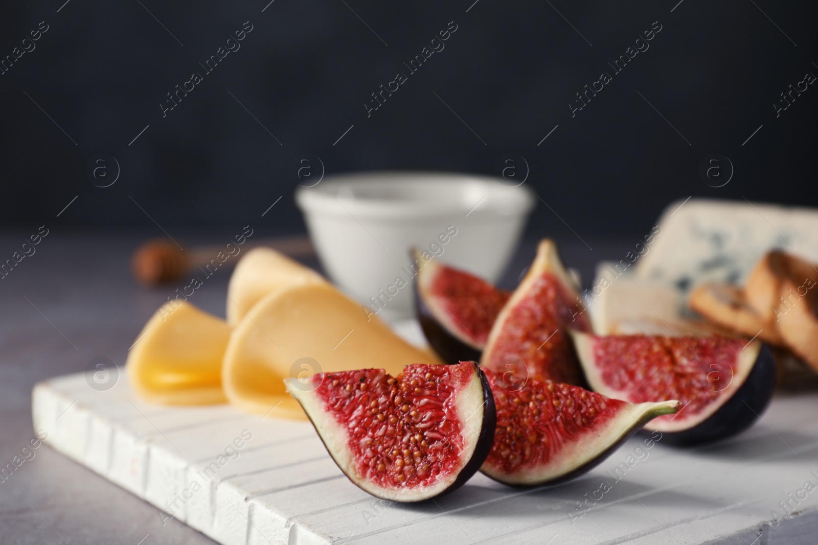 Photo of Wooden board with ripe fig slices on grey table, closeup