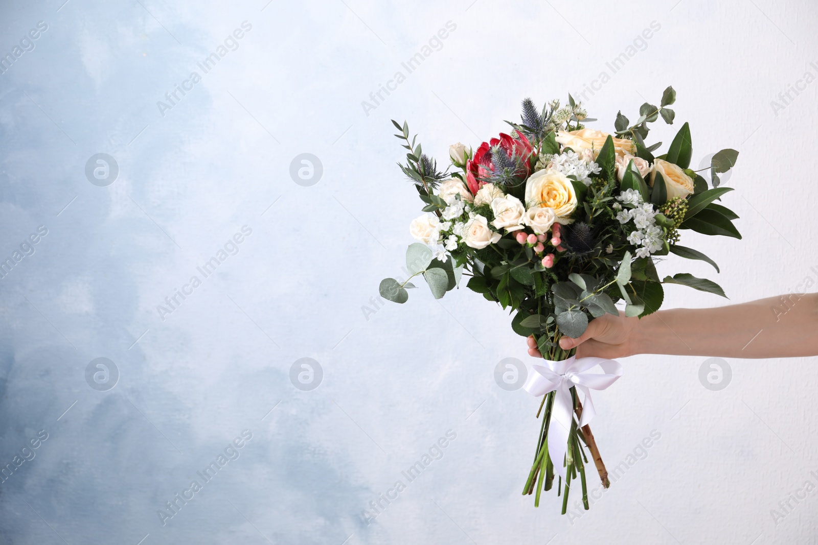 Photo of Woman with bouquet of beautiful roses on light blue background, closeup. Space for text