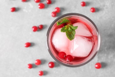 Photo of Tasty cranberry juice with ice cubes in glass and fresh berries on light grey table, top view