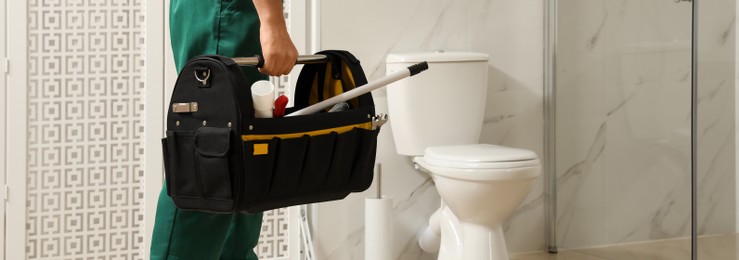 Professional plumber with toolbox near toilet bowl in bathroom, closeup. Banner design