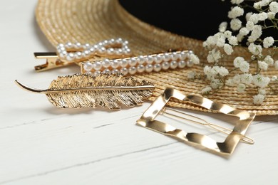 Stylish hair clips and hat on white wooden table