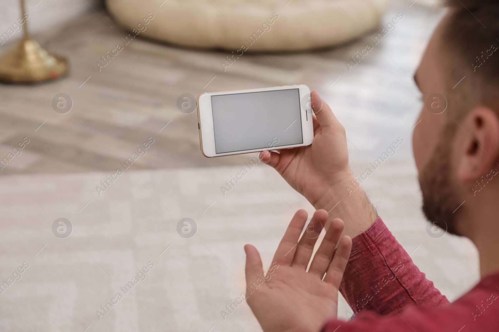 Photo of Young man using video chat on smartphone at home, closeup. Space for design