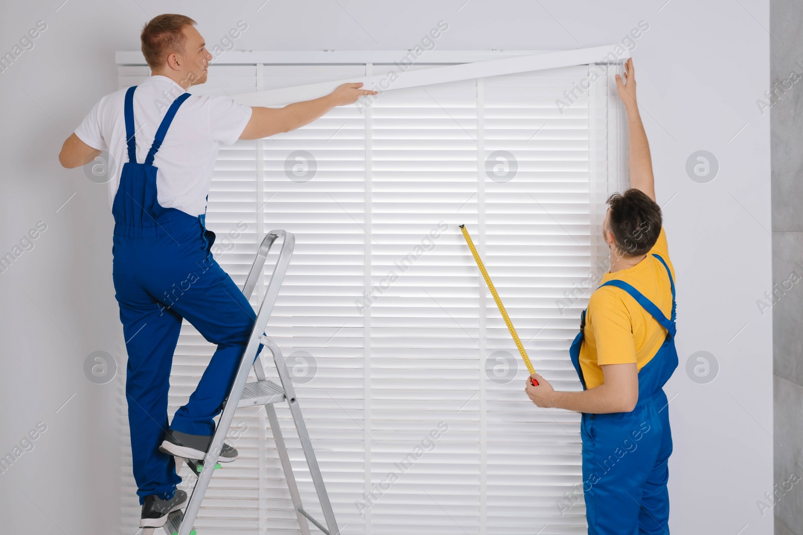 Photo of Workers in uniforms installing horizontal window blinds indoors