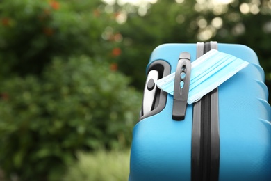 Stylish blue suitcase with protective mask outdoors, space for text. Travelling during coronavirus pandemic