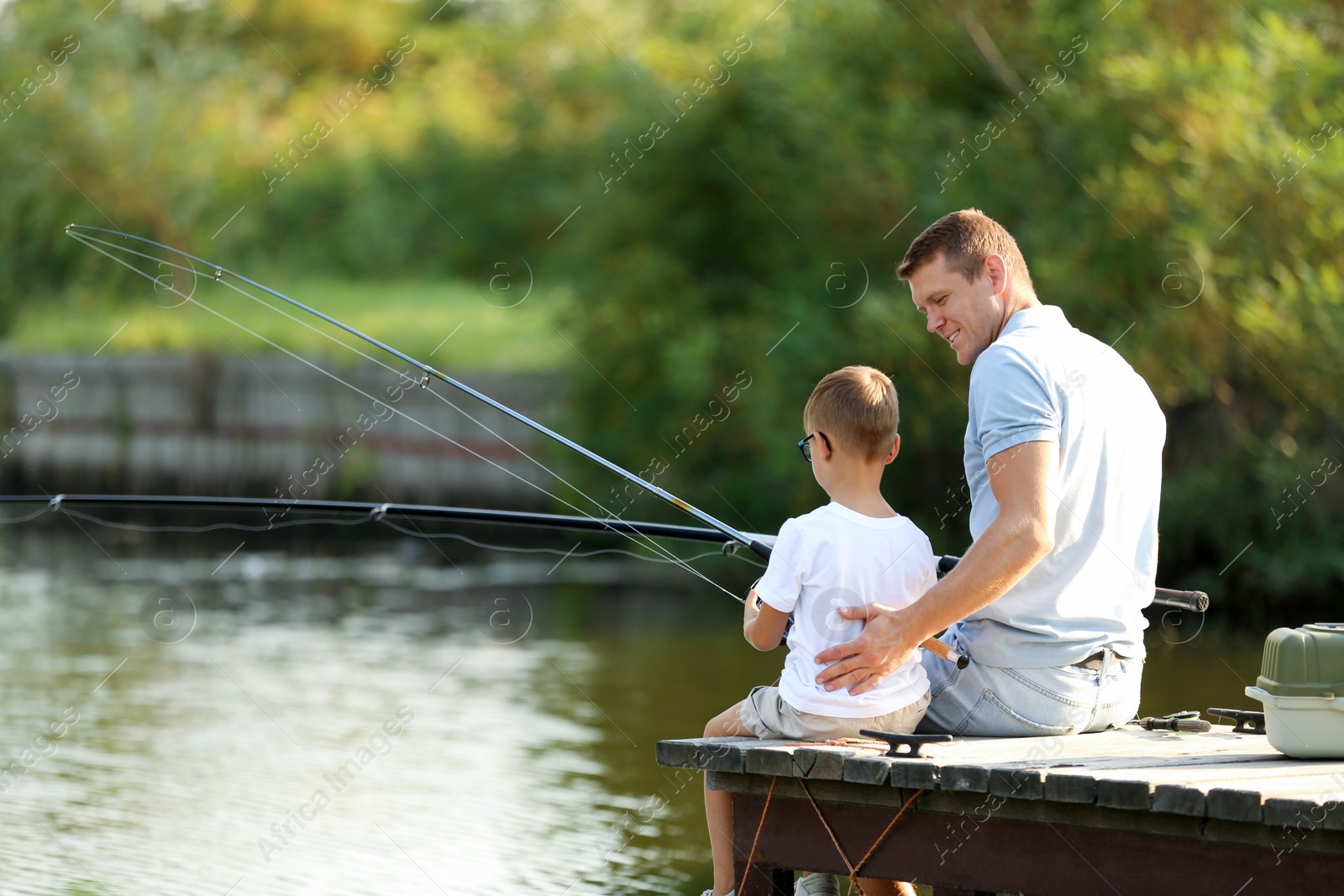 Photo of Dad and son fishing together on sunny day. Space for text