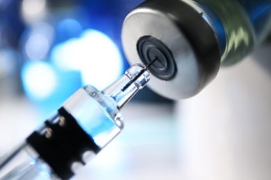 Filling syringe with vaccine from vial on blurred background, closeup