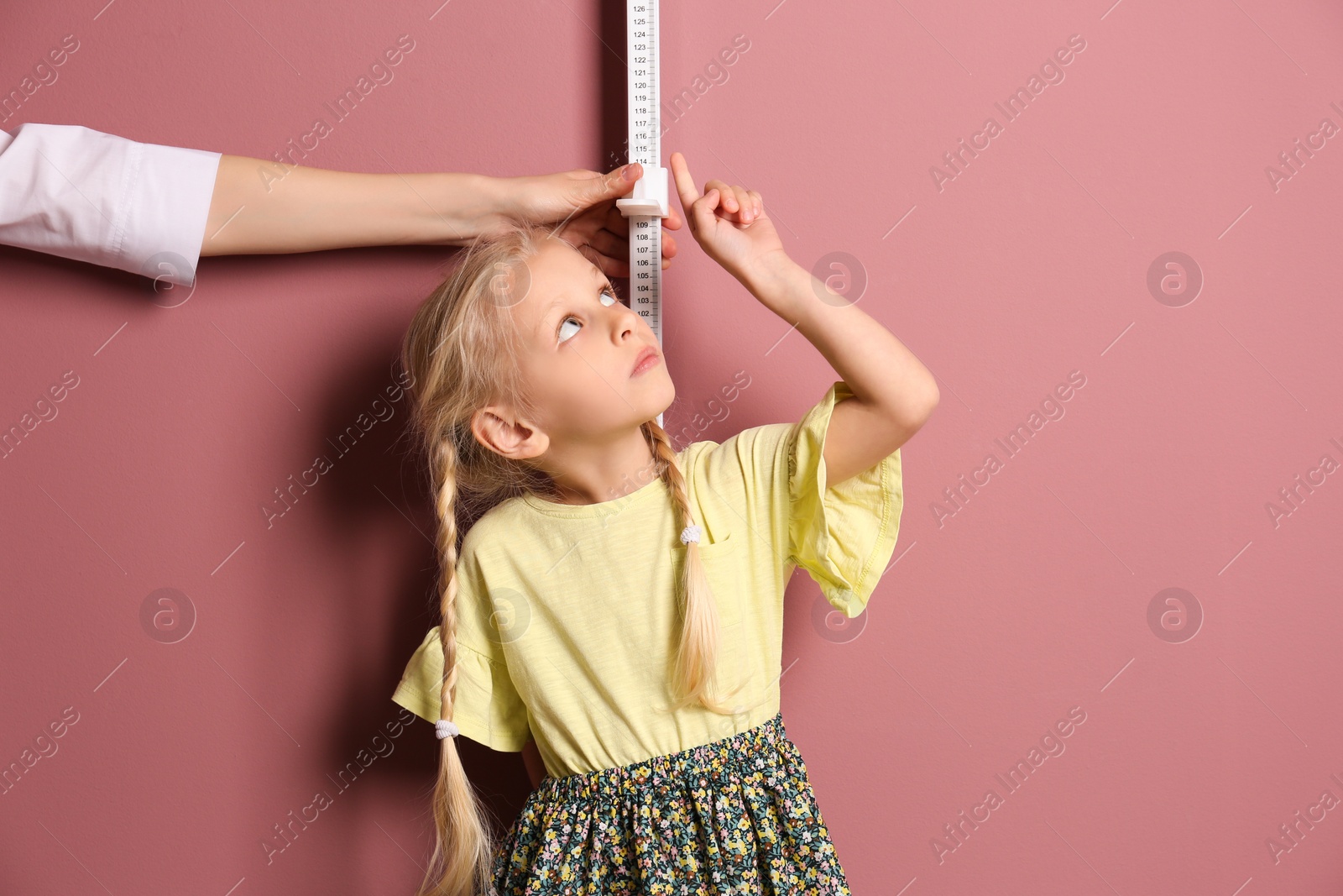 Photo of Doctor measuring little girl's height on color background