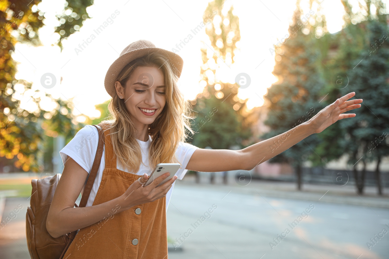 Photo of Young woman with smartphone catching taxi on city street