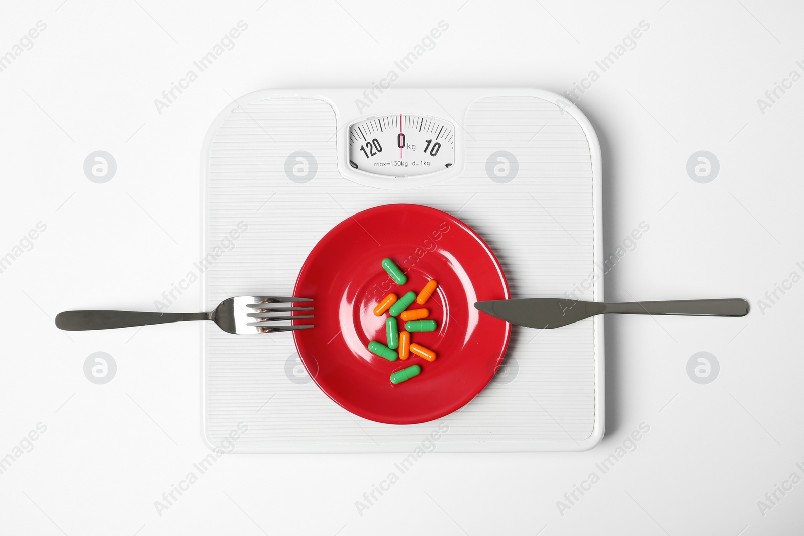 Photo of Scales with plate of weight loss pills and cutlery on white background, top view