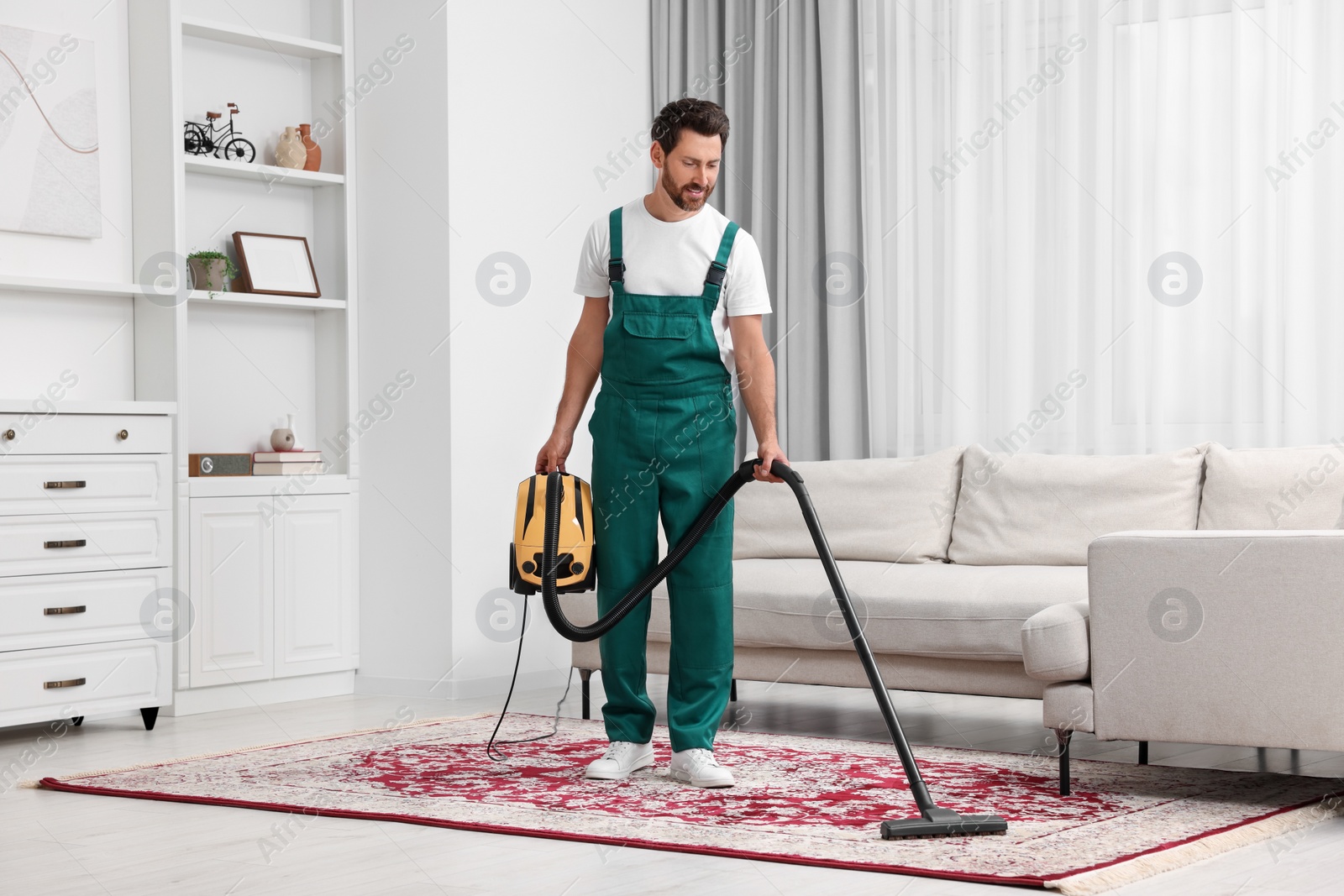 Photo of Dry cleaner's employee hoovering carpet with vacuum cleaner in room