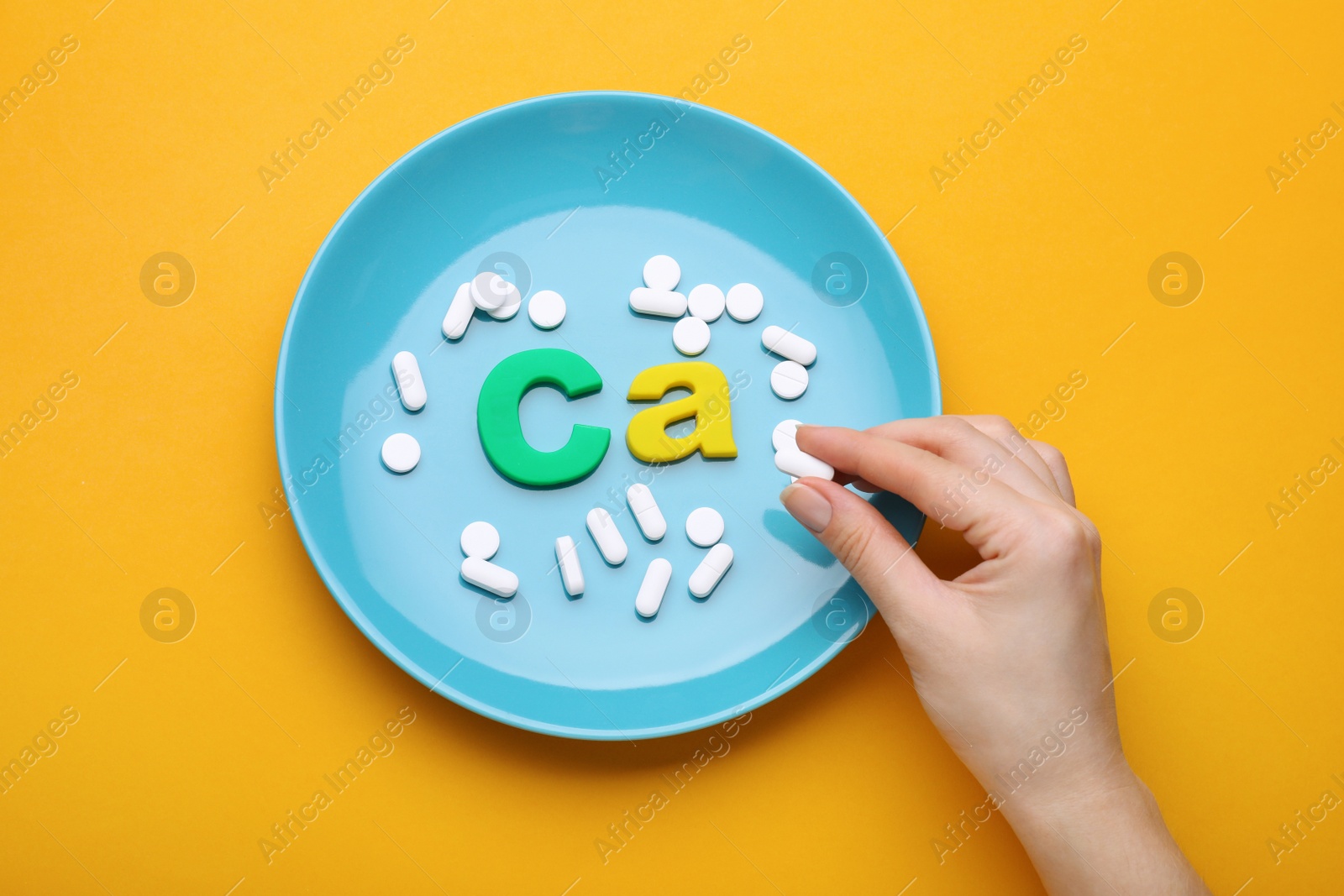 Photo of Woman, plate with pills and calcium symbol made of colorful letters on orange background, top view